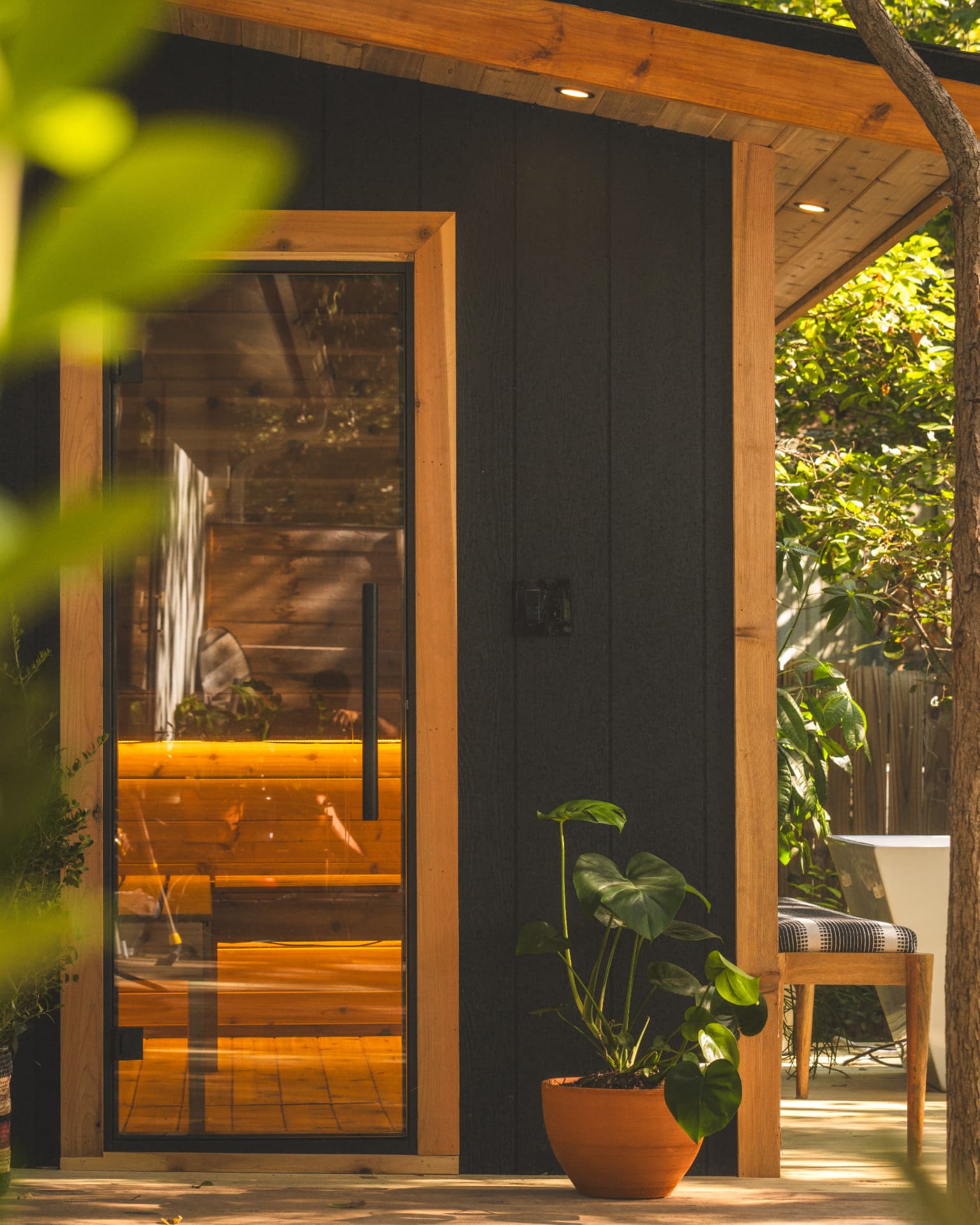 Glass sauna door in a cedar frame glowing warm against blackened cedar cladding