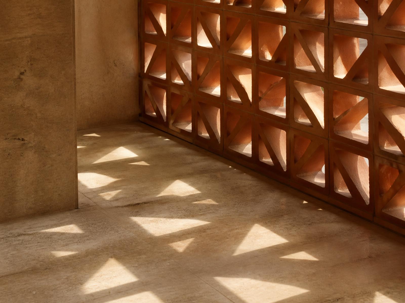 Structural terracotta breeze-block screen casting geometric daylight patterns onto a limestone floor
