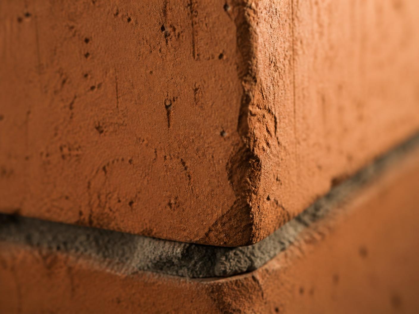 Macro detail of a hand-pressed terracotta block edge and lime mortar joint in raking light