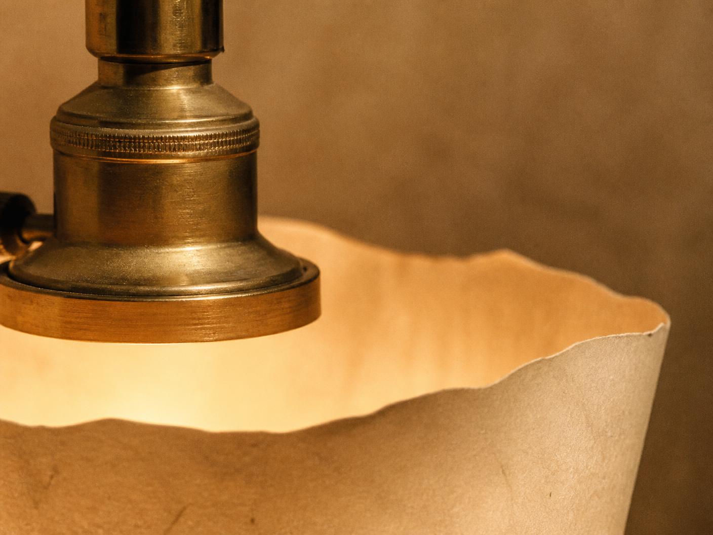 Close detail of a raw brass lamp fitting against the torn edge of a handmade paper shade
