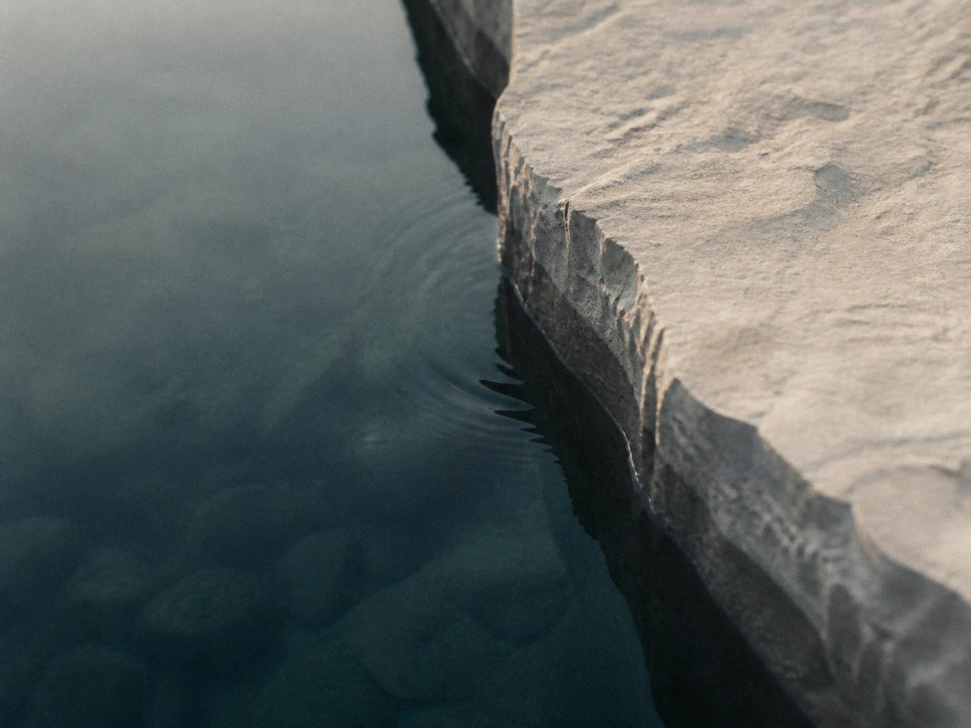 Still cold water meeting the chiselled limestone edge of a plunge bath